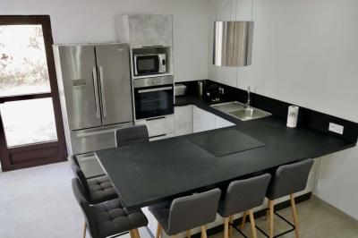 Salon avec canapé beige, fauteuils, table basse, télévision, cheminée en pierre et plafond avec poutres apparentes.