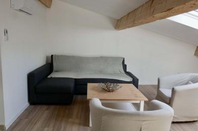 Salon avec canapé beige, fauteuils, table basse, télévision, cheminée en pierre et plafond avec poutres apparentes.