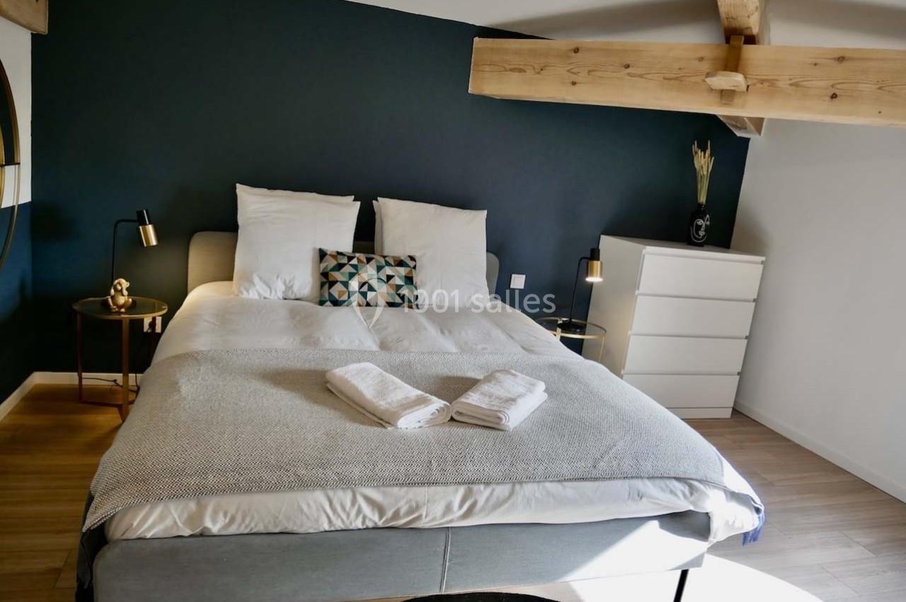 Lit double avec draps blancs, coussins décoratifs, tables de chevet et poutre apparente dans une chambre moderne.