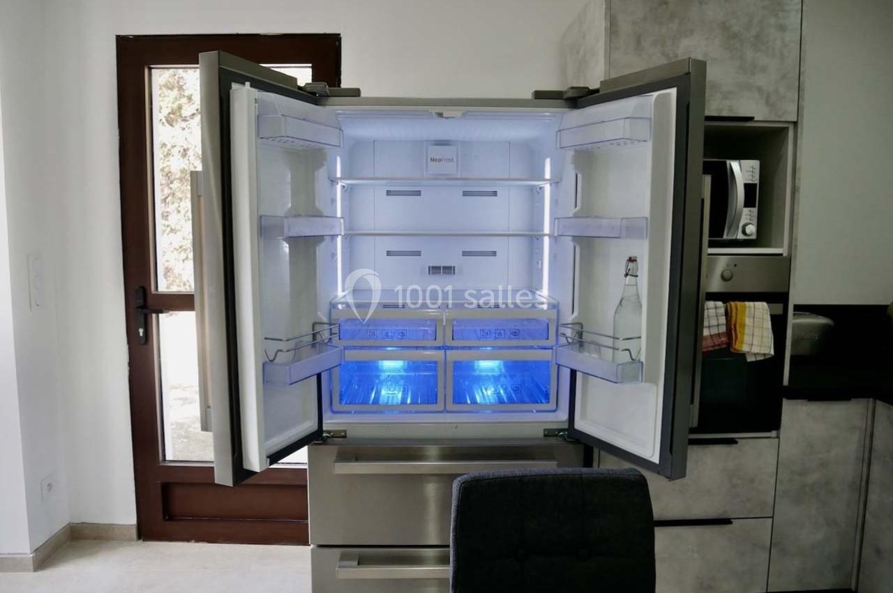 Réfrigérateur moderne à portes ouvertes, montrant des étagères vides et un éclairage intérieur bleu.