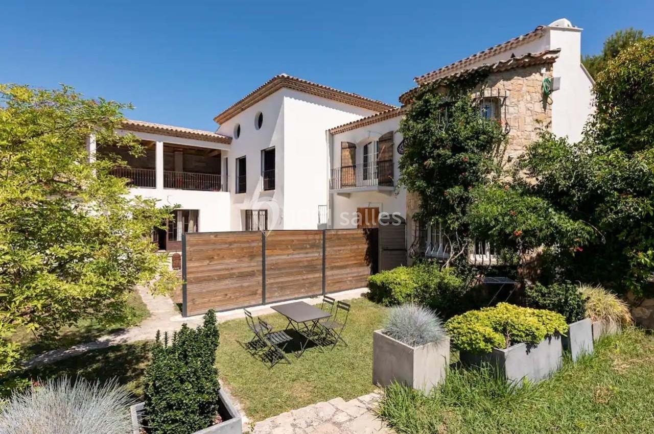 Façade d'une maison méditerranéenne avec jardin, terrasse, mobilier d'extérieur et végétation abondante.