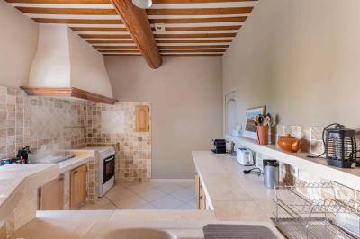 Salon avec canapé beige, fauteuils, table basse, télévision, cheminée en pierre et plafond avec poutres apparentes.