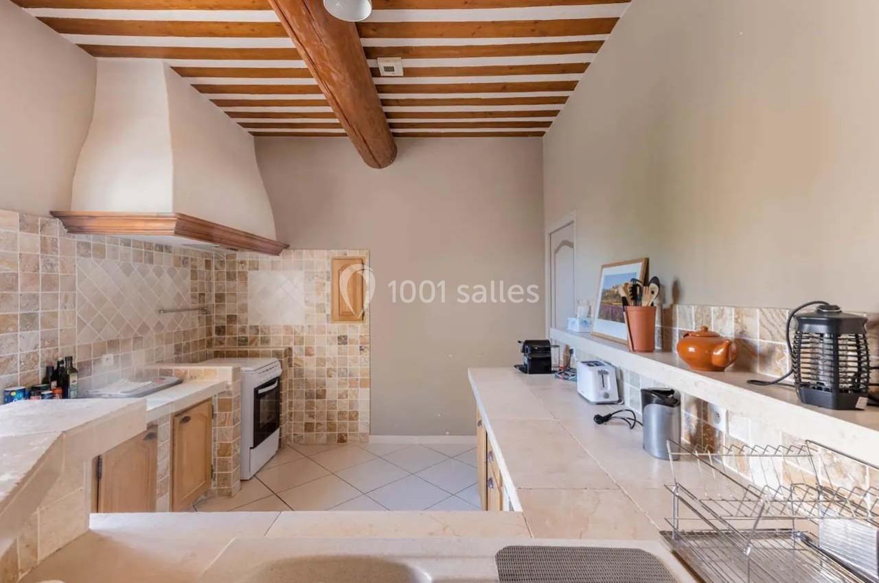 Cuisine lumineuse avec poutres apparentes, plan de travail en pierre, électroménagers et crédence en carreaux beige.