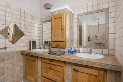 Salon avec canapé beige, fauteuils, table basse, télévision, cheminée en pierre et plafond avec poutres apparentes.