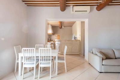 Salon avec canapé beige, fauteuils, table basse, télévision, cheminée en pierre et plafond avec poutres apparentes.