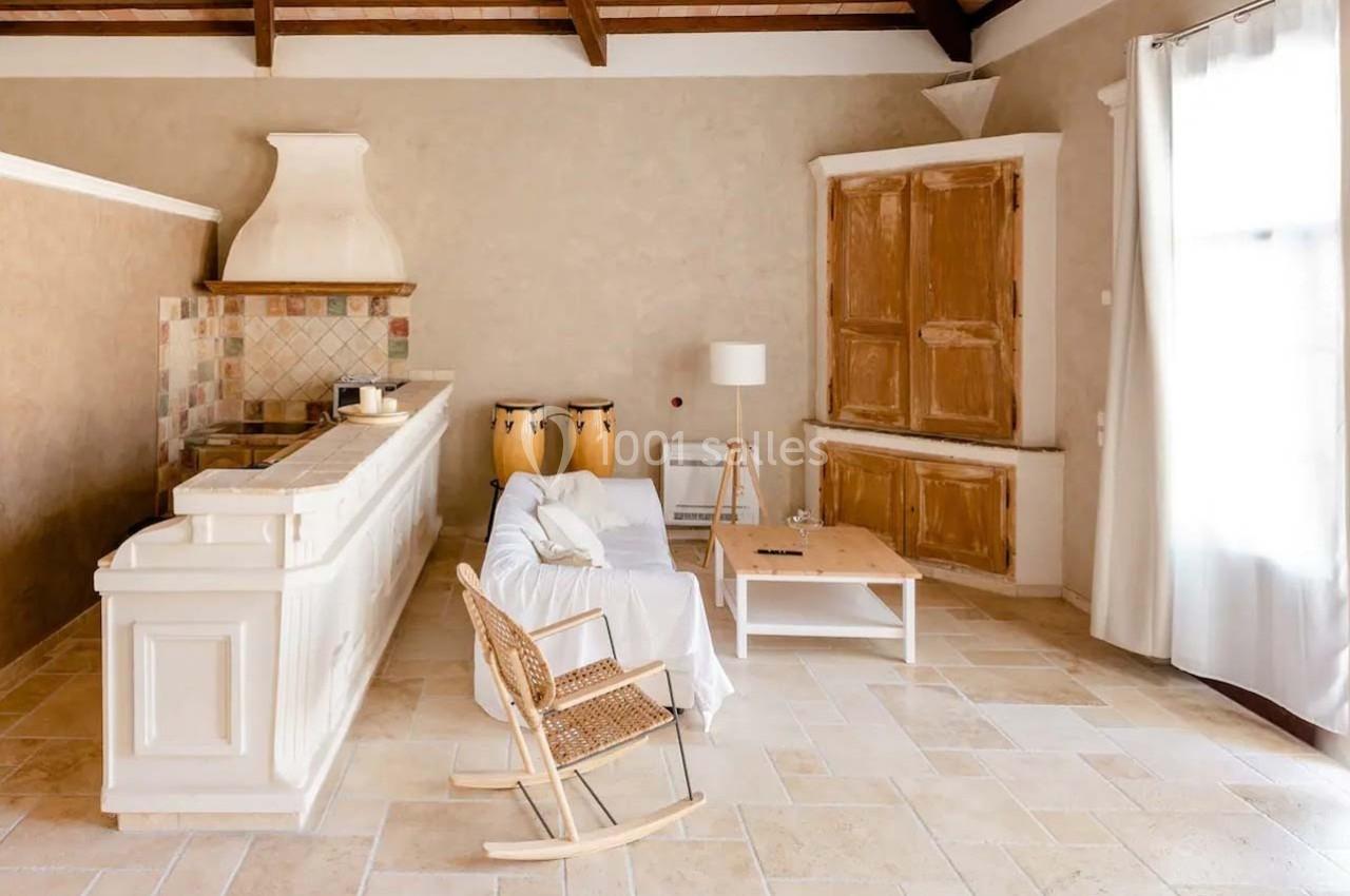 Salon lumineux avec canapé blanc, rocking-chair en bois, table basse, cuisine ouverte et murs beige clair.