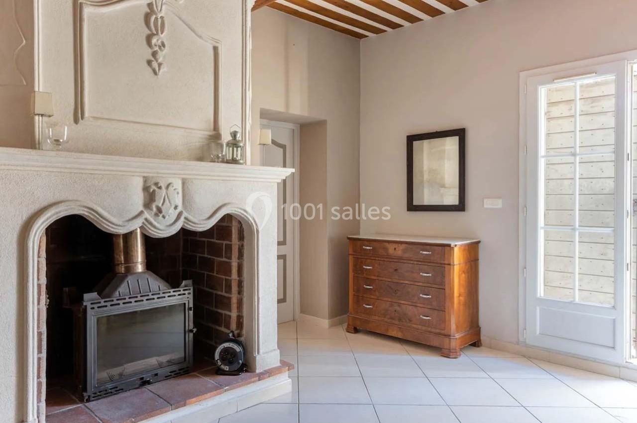 Cheminée en pierre avec insert, meuble en bois et porte vitrée donnant sur un espace lumineux au sol carrelé.