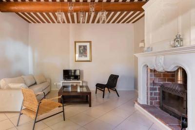 Salon avec canapé beige, fauteuils, table basse, télévision, cheminée en pierre et plafond avec poutres apparentes.