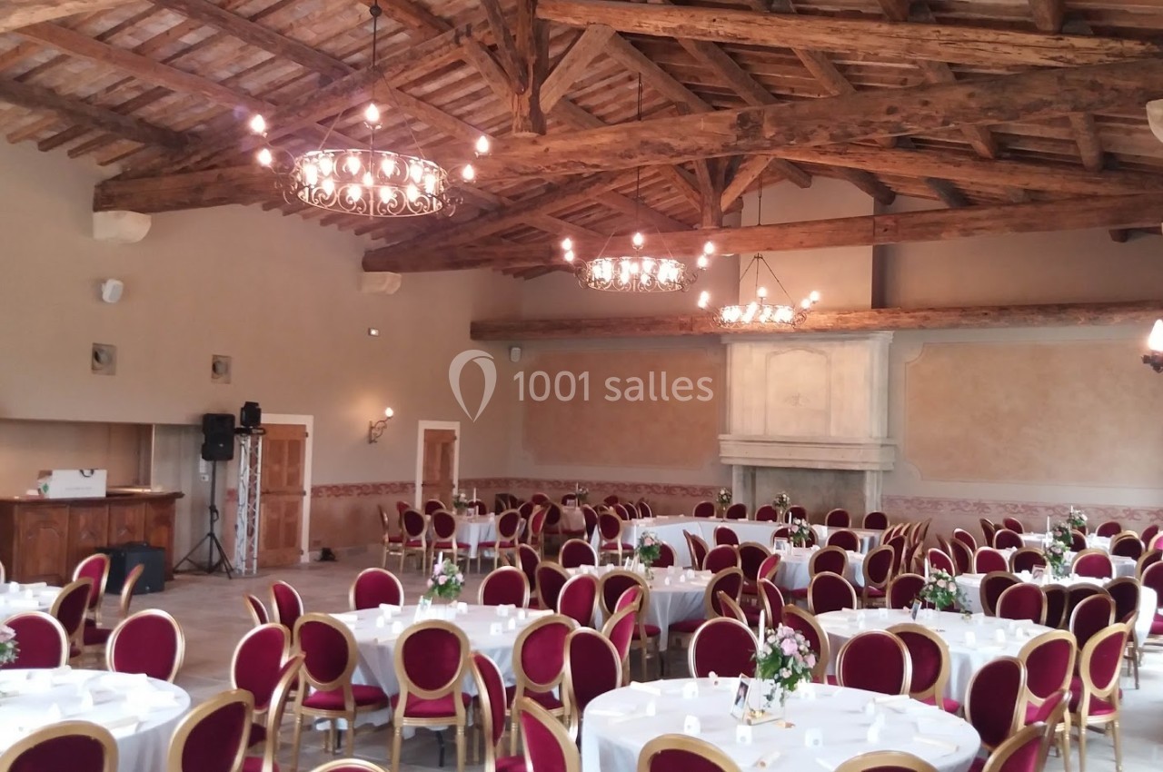 Salle de réception avec poutres apparentes, tables rondes dressées et chaises rouges, décorée pour un événement.