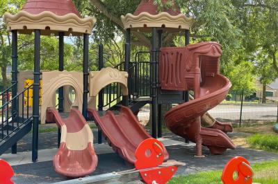 Étang entouré d'arbres et de buissons sous la neige, avec un lampadaire et des bancs dans un paysage hivernal.