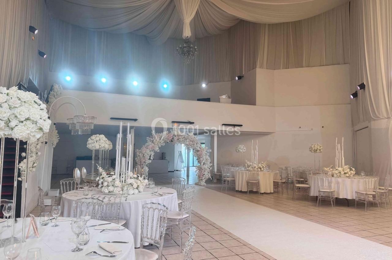 Salle de réception élégante décorée de fleurs blanches, avec tables dressées et éclairage tamisé.