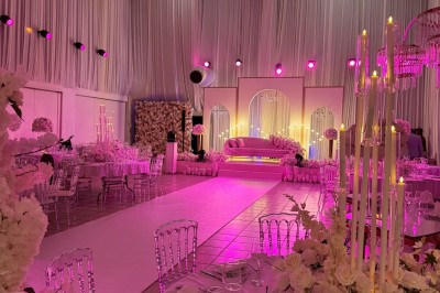 Salle de réception décorée avec des tables rondes, des chaises transparentes et des arrangements floraux blancs sous un…