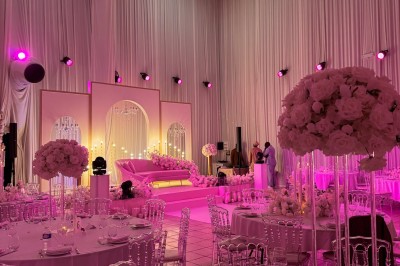 Salle de réception décorée avec des tables rondes, des chaises transparentes et des arrangements floraux blancs sous un…