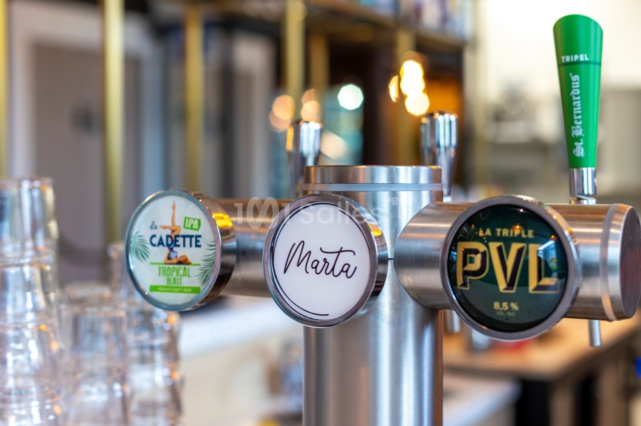 Tireuse à bière avec trois robinets affichant les logos de différentes marques dans un bar lumineux.