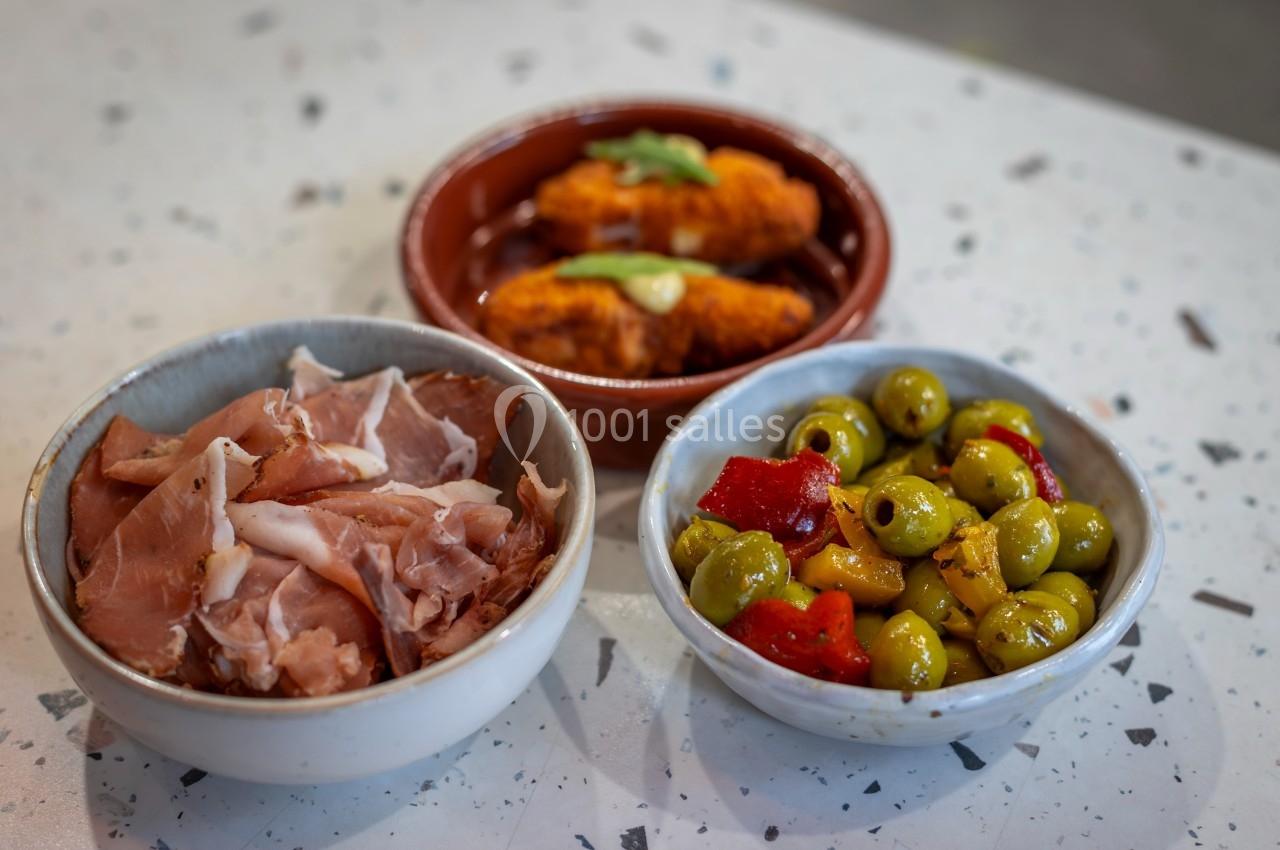 Assortiment de tapas avec jambon cru, olives marinées aux poivrons et croquettes servies dans des bols.