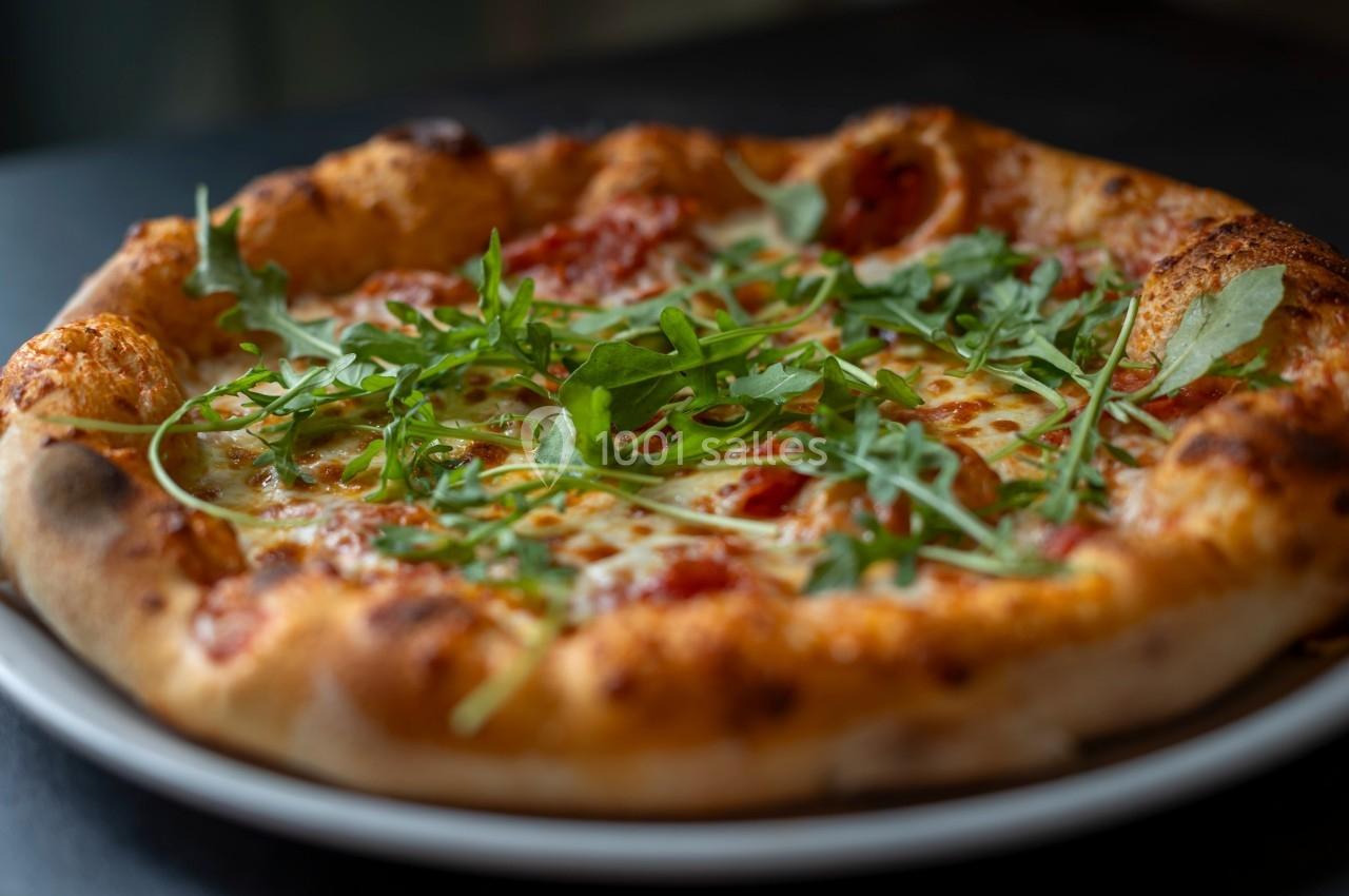 Pizza garnie de roquette fraîche, sauce tomate et fromage fondu, servie sur une assiette blanche.