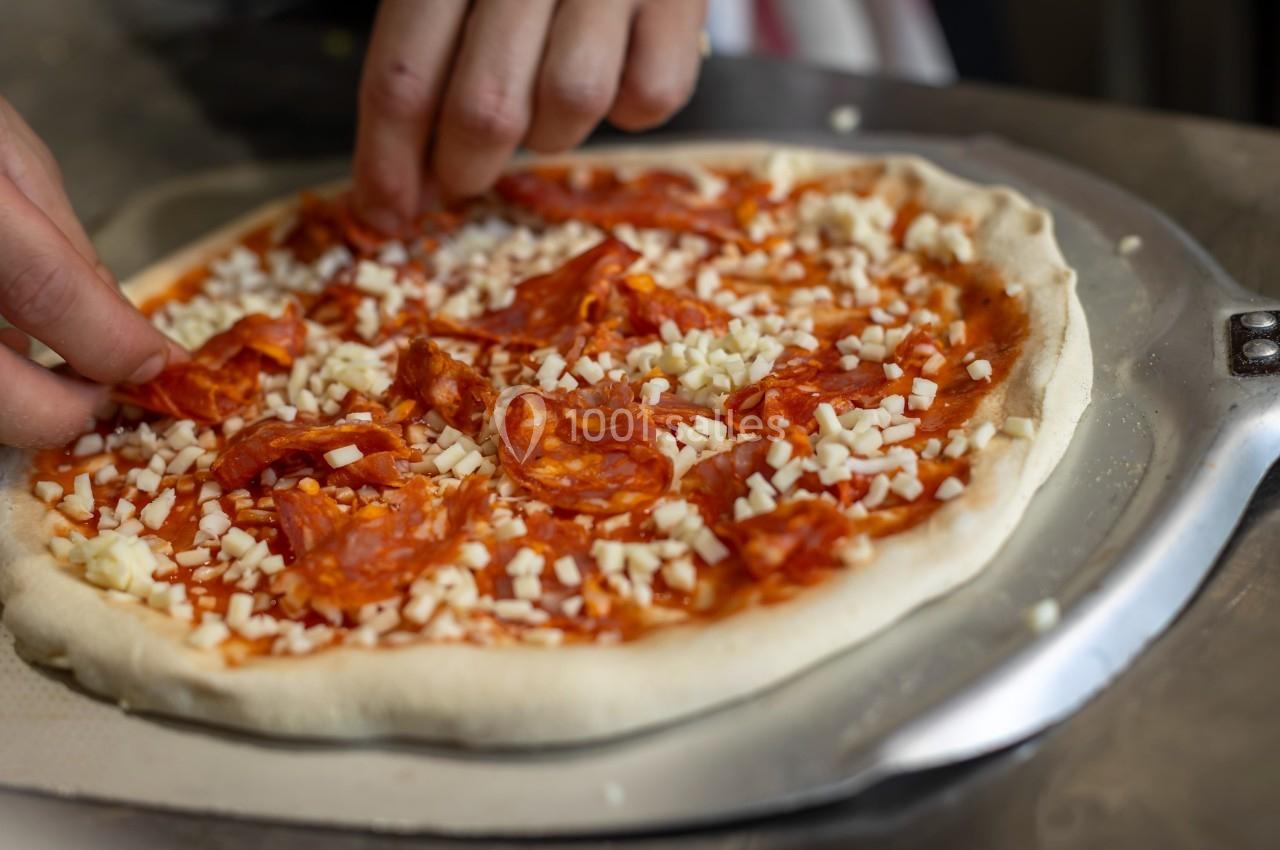 Une personne garnit une pizza avec des tranches de chorizo et du fromage râpé sur une pâte crue.