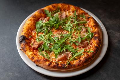 Miniature Location salle Lille (Nord) - Marta Bar Restaurant #8 Préparation d'une pizza avec des mains ajoutant des tranches de chorizo sur une pâte garnie de sauce tomate et fromage râpé.
