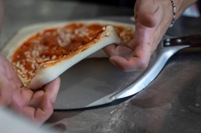 Miniature Location salle Lille (Nord) - Marta Bar Restaurant #11 Préparation d'une pizza avec des mains ajoutant des tranches de chorizo sur une pâte garnie de sauce tomate et fromage râpé.