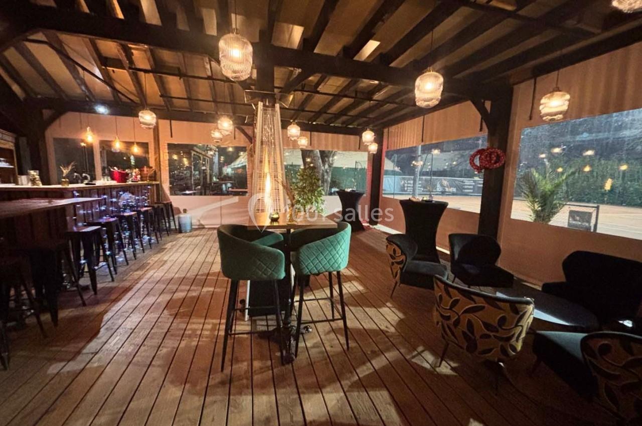 Terrasse couverte en bois avec tables, chaises, lampes suspendues et chauffage central, ambiance chaleureuse en soirée.