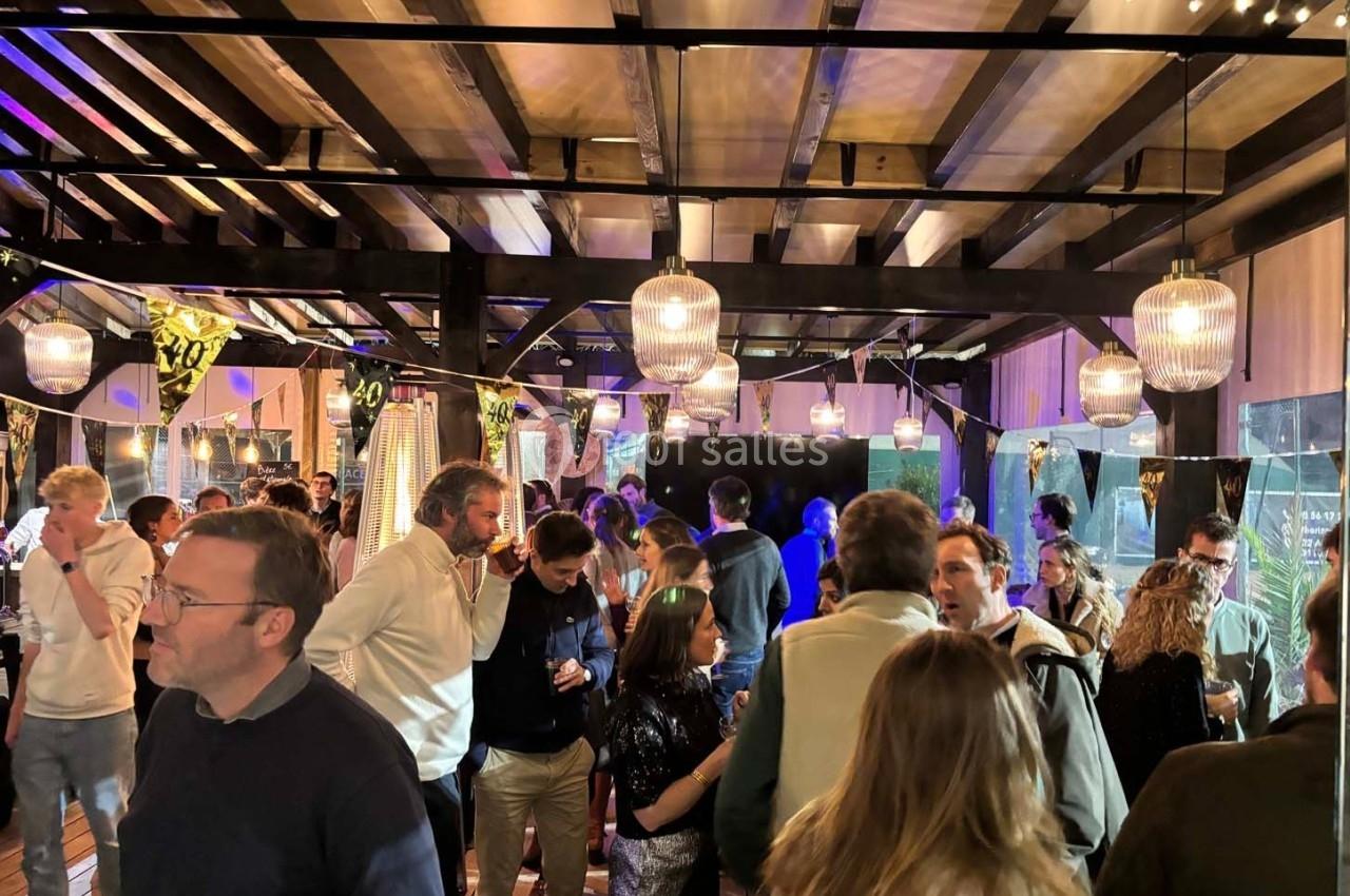 Des personnes discutent et socialisent dans un espace intérieur éclairé par des guirlandes et des suspensions lumineuses.