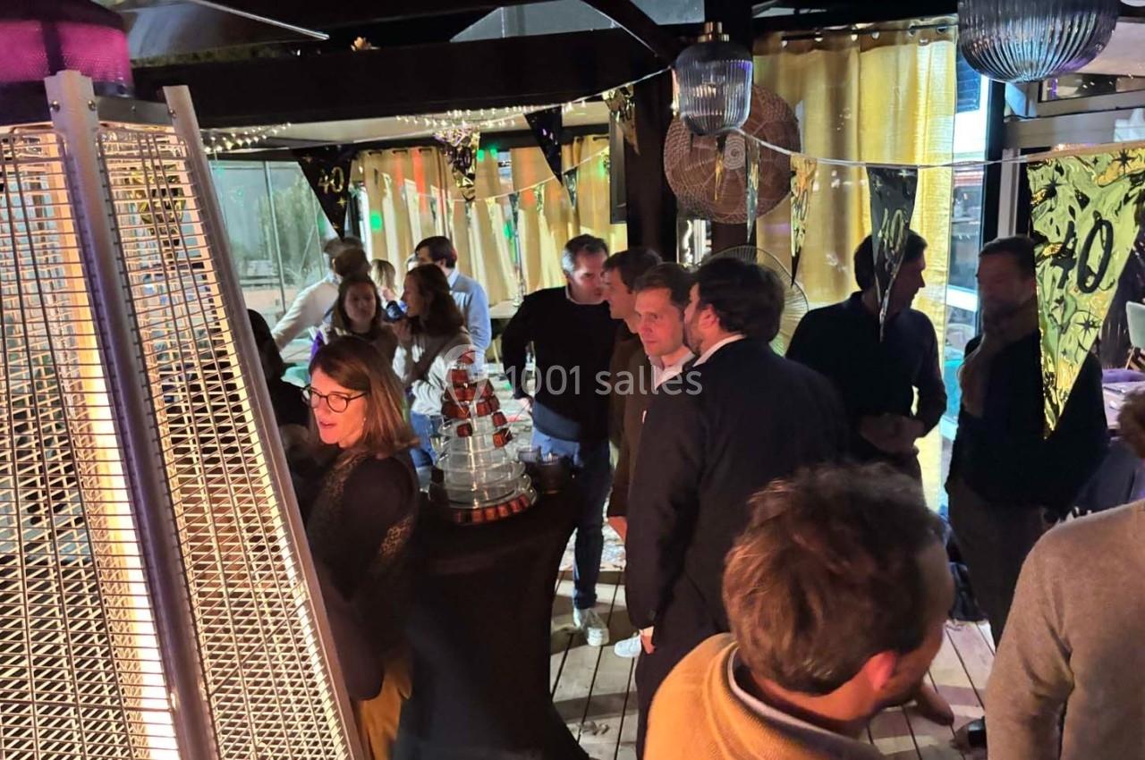 Des personnes discutent dans un espace intérieur décoré, éclairé par des lampes et un chauffage d'extérieur.