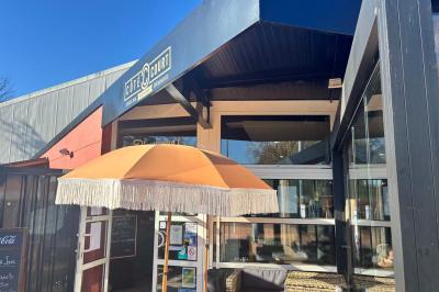 Miniature Location salle Le Bouscat (Gironde) - Côté Court #40 Entrée d'un café avec une grande terrasse, un parasol orange et des meubles en osier sous un ciel bleu.