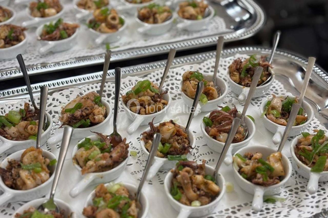 Petites coupelles blanches contenant des fruits de mer cuisinés, garnis de ciboulette, présentées sur un plateau argenté.