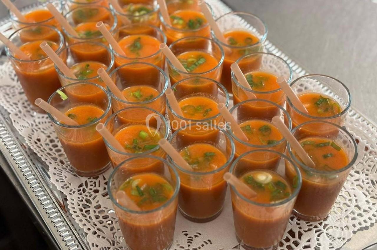 Petits verres de gaspacho rouge garnis de ciboulette, disposés sur un plateau avec napperon blanc.