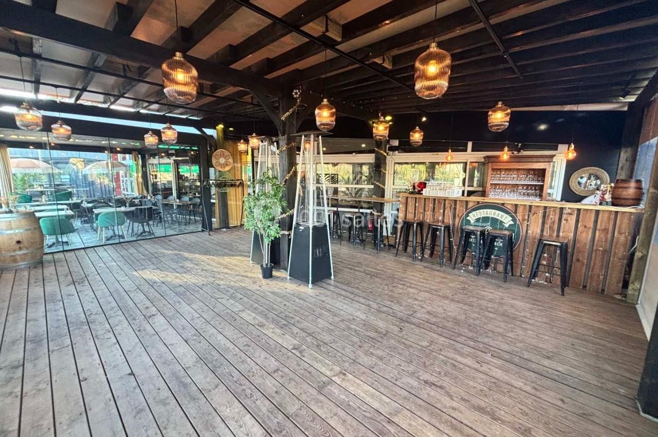 Terrasse en bois couverte avec bar, tabourets hauts, tables, chaises et éclairage suspendu dans une ambiance chaleureuse.