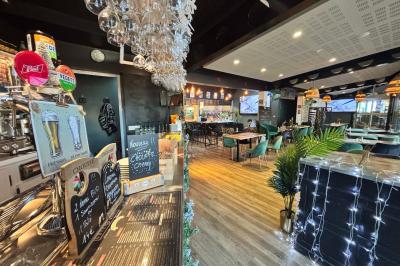 Miniature Location salle Le Bouscat (Gironde) - Côté Court #26 Entrée d'un café avec une grande terrasse, un parasol orange et des meubles en osier sous un ciel bleu.