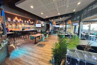 Miniature Location salle Le Bouscat (Gironde) - Côté Court #12 Entrée d'un café avec une grande terrasse, un parasol orange et des meubles en osier sous un ciel bleu.