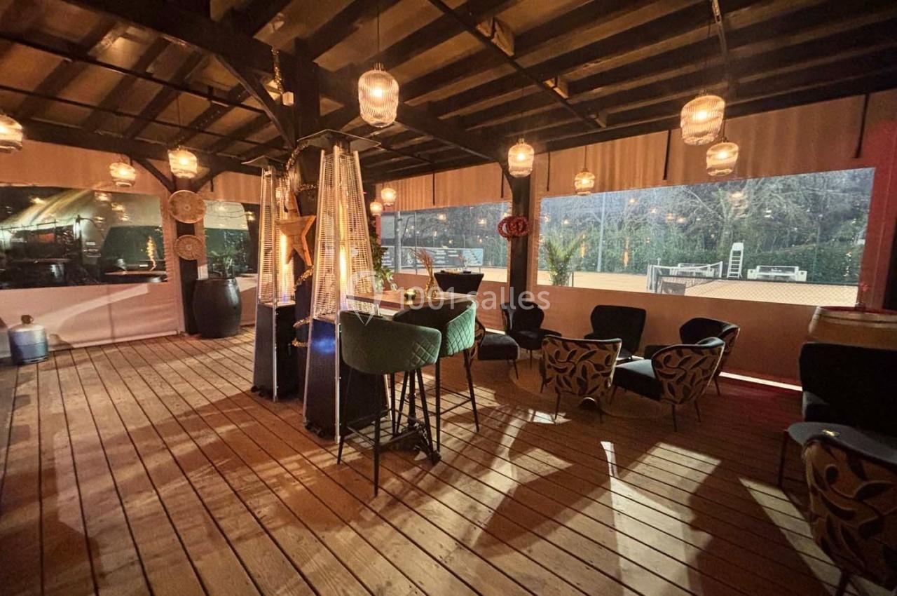 Terrasse couverte en bois avec éclairage chaleureux, mobilier varié et vue sur un extérieur nocturne.