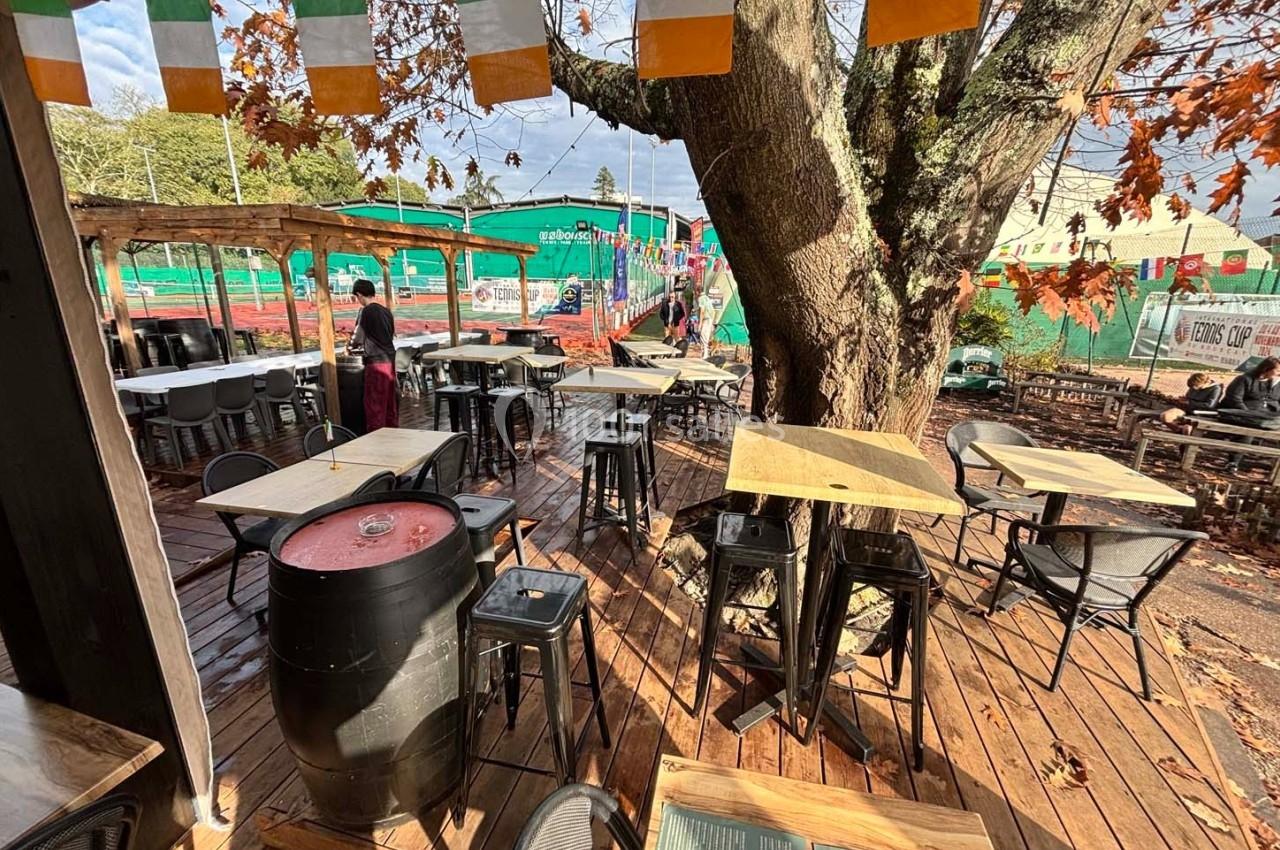 Terrasse en bois avec tables et chaises, décorée de fanions colorés, près d'un arbre en automne.