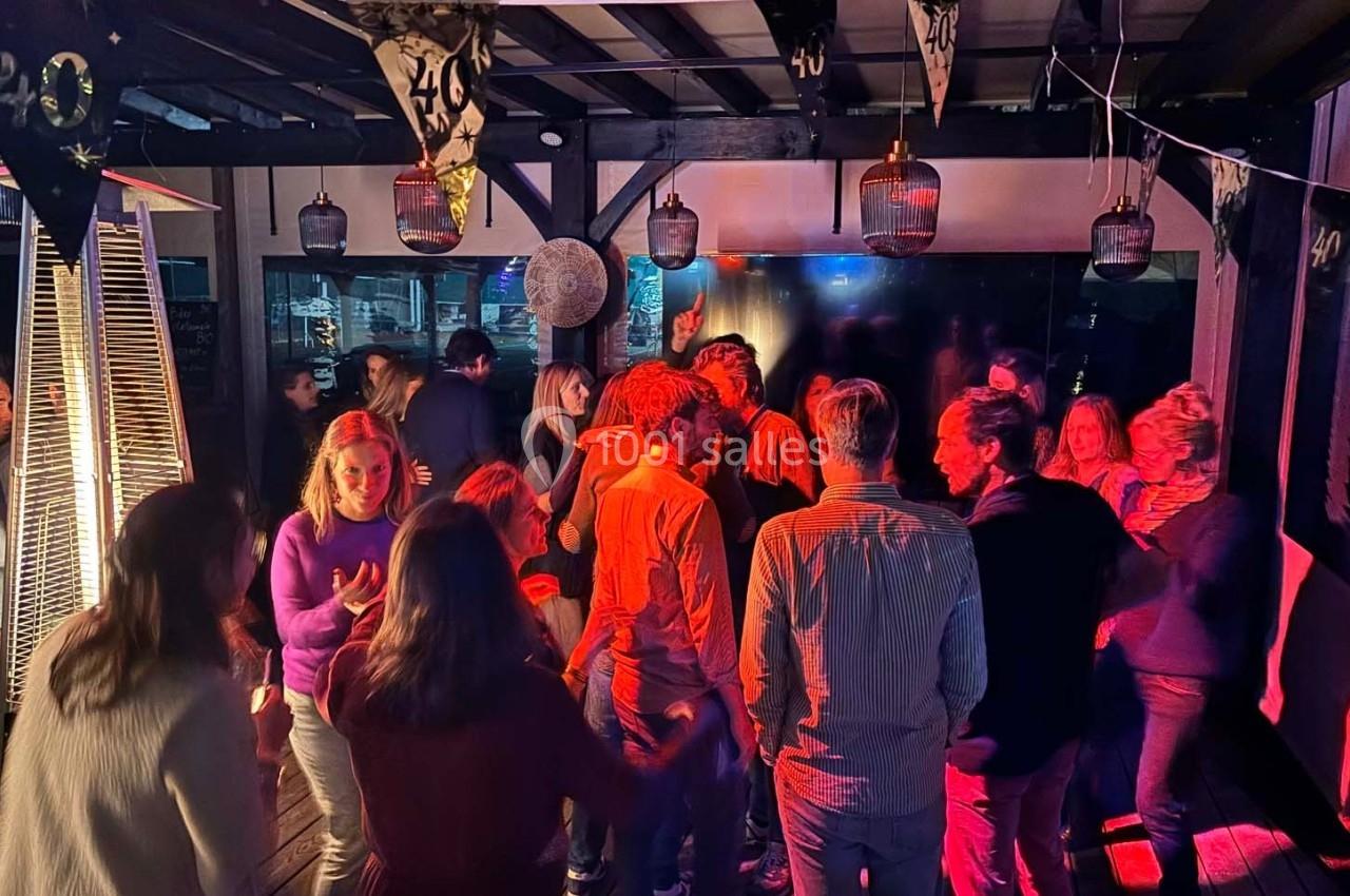 Groupe de personnes dans une ambiance festive avec éclairage coloré, décorations suspendues et chauffage extérieur.
