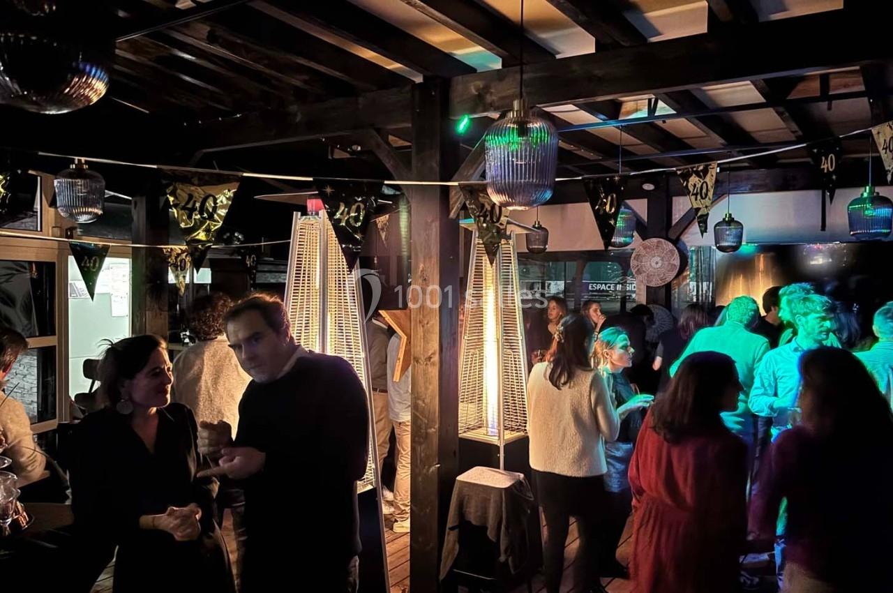 Des personnes discutent et dansent dans un espace intérieur faiblement éclairé avec des décorations festives et des…