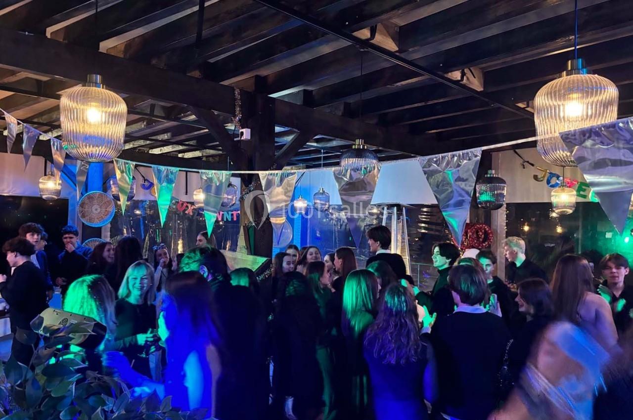 Groupe de personnes dans une salle décorée, éclairée par des lumières colorées, lors d'un événement festif en soirée.