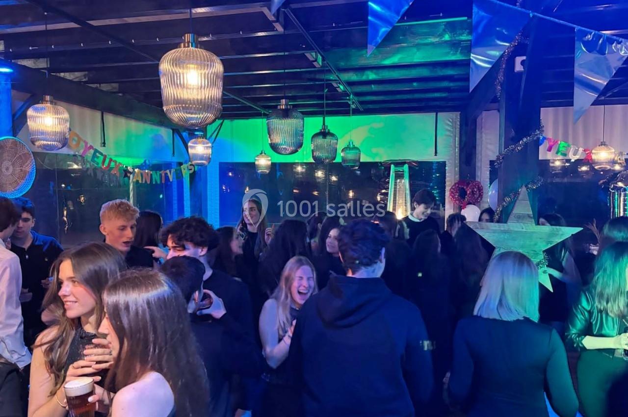 Des personnes dansent et discutent lors d'une soirée festive éclairée par des lumières colorées et des décorations…