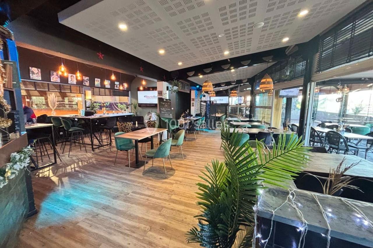 Intérieur d'un restaurant moderne avec tables, chaises, plantes décoratives et éclairage chaleureux.