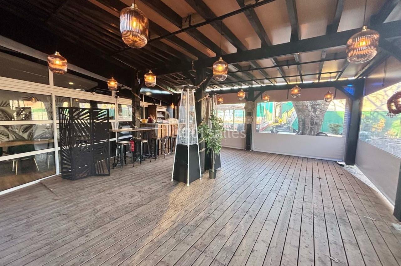 Terrasse couverte en bois avec des tables hautes, des lampes suspendues et des chauffages d'extérieur.