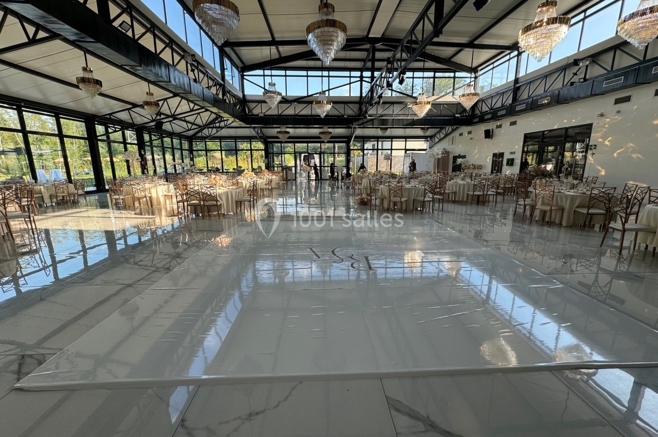 Salle de réception lumineuse avec tables dressées, chaises élégantes et piste de danse centrale sous des lustres.