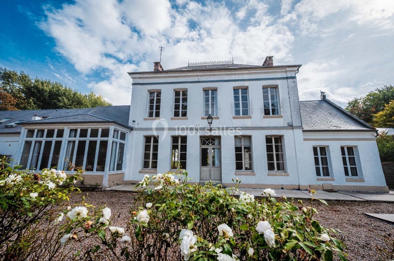 Façade d'une maison blanche à deux étages avec des fenêtres symétriques, entourée de rosiers en fleurs.