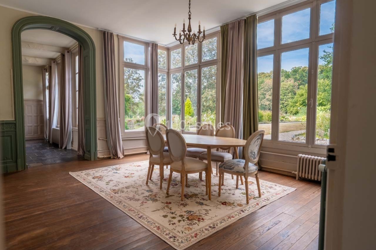 Salle à manger lumineuse avec table ronde, chaises élégantes, grandes fenêtres donnant sur un jardin verdoyant.