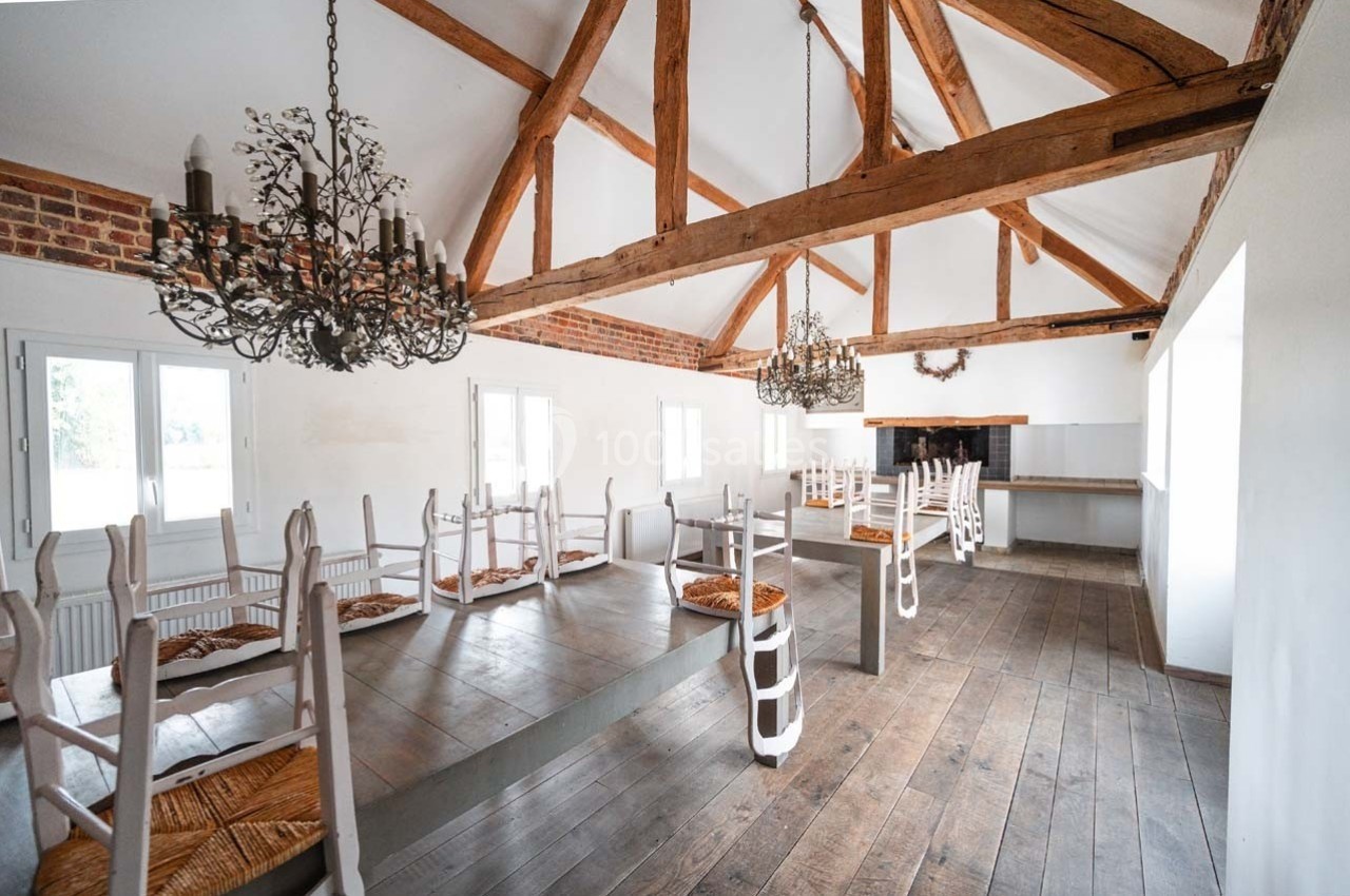 Salle lumineuse avec poutres apparentes, chaises retournées sur des tables en bois et un comptoir au fond.