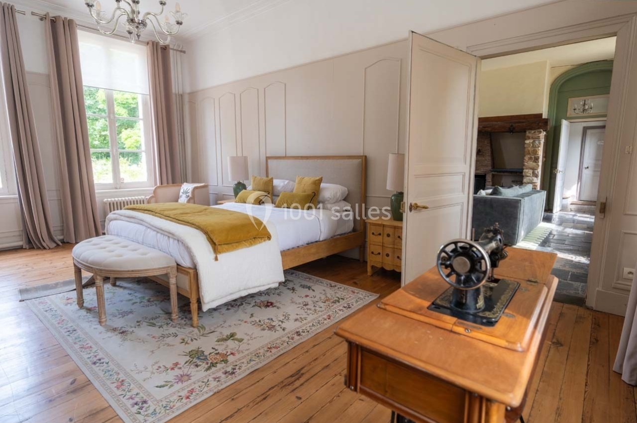 Chambre lumineuse avec lit double, coussins colorés, parquet en bois, tapis floral et machine à coudre ancienne au premier…