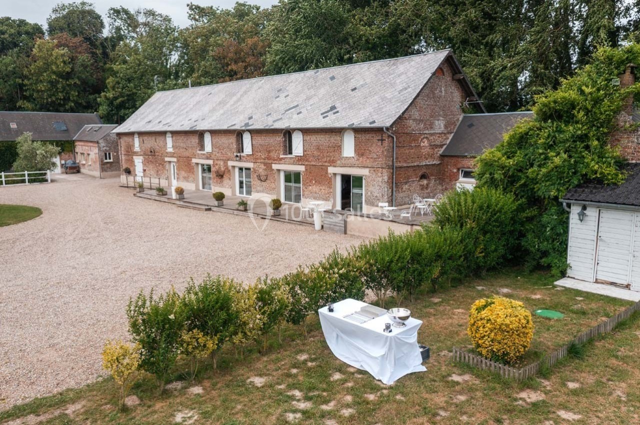 Bâtiment en briques avec toit en ardoise, entouré de végétation et d'une cour gravillonnée, table dressée au premier plan.