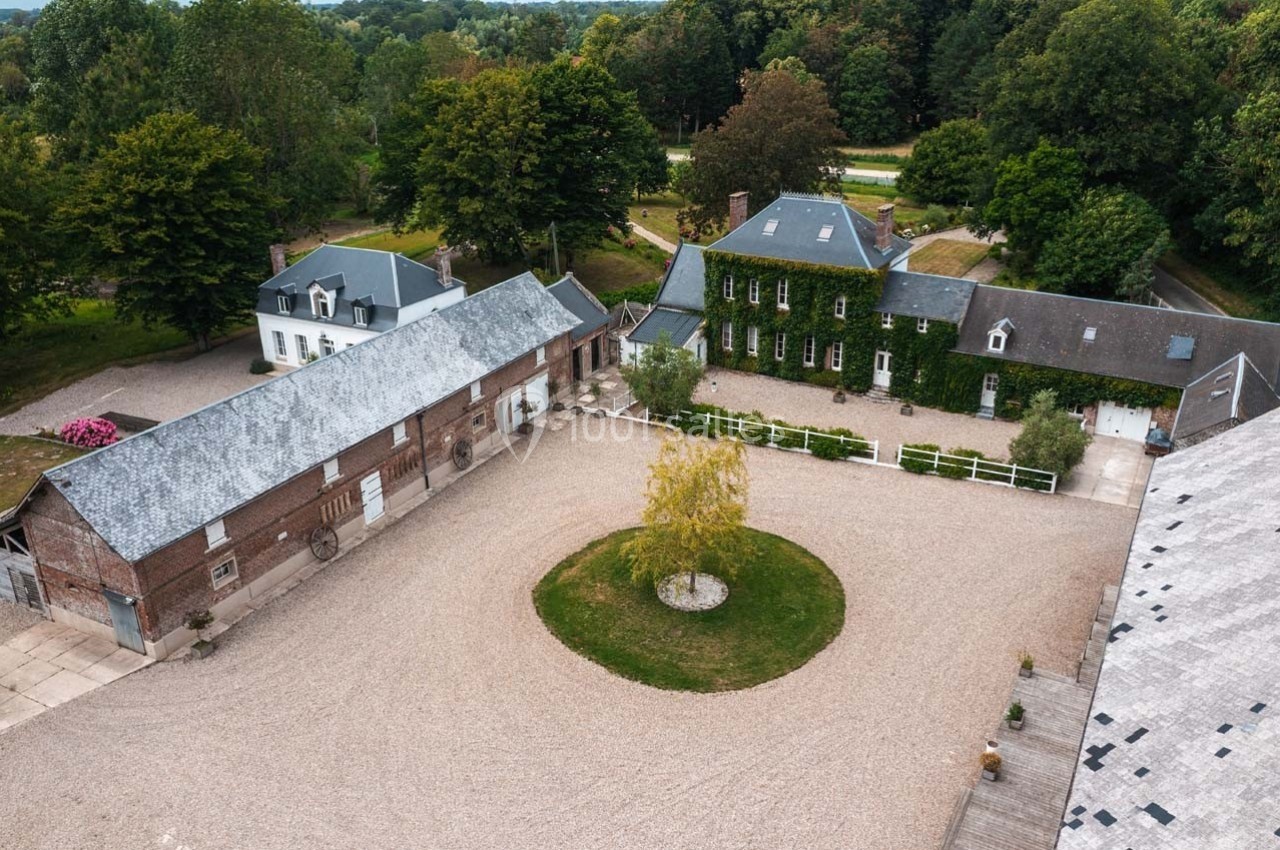 Vue aérienne d'une cour pavée entourée de bâtiments anciens en briques et toits d'ardoise, avec un arbre central.