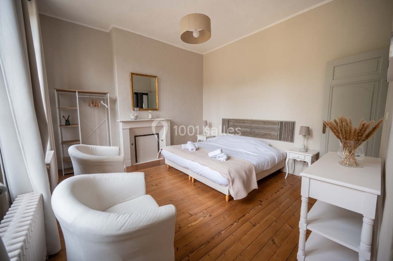Chambre lumineuse avec lit double, fauteuils blancs, parquet en bois et décoration sobre dans des tons neutres.