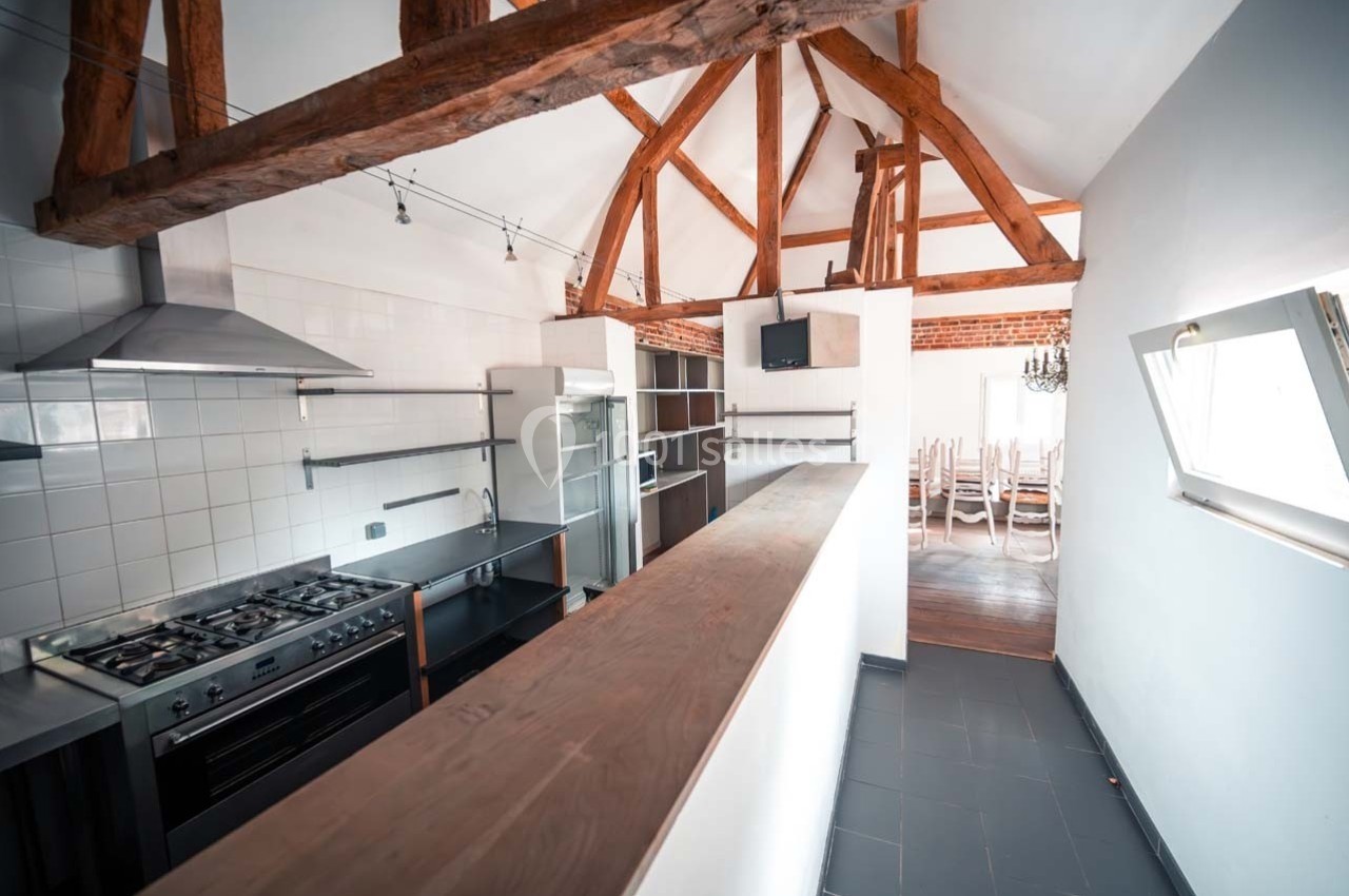 Cuisine avec poutres apparentes, équipée d'une cuisinière, d'étagères métalliques et ouverte sur une salle à manger…