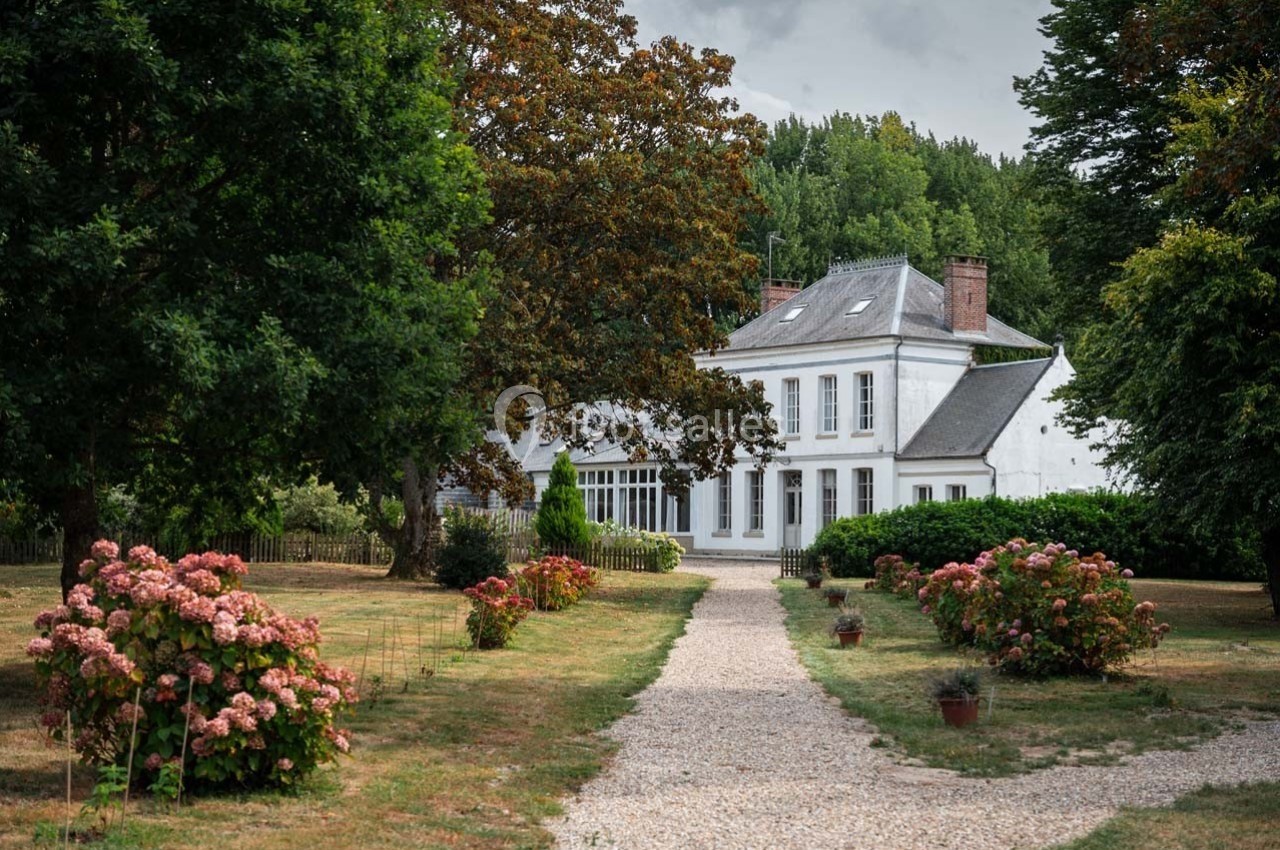 Allée gravillonnée bordée d'hortensias menant à une maison blanche entourée d'arbres et de verdure.